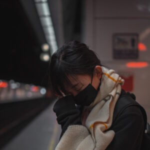 Eine müde Chinesin steht am Bahnhof und blickt erschöpft nach unten.